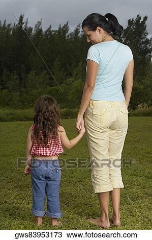 Stock Image - Rear view of a young woman holding her daughter's hand and standing on the lawn. Fotosearch