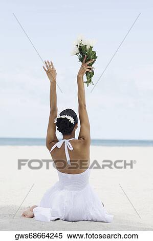 Rear view of a young woman sitting and holding flowers on the beach View Large Photo Image Stock Photography - Rear view of a young woman sitting and holding flowers on the beach. Fotosearch