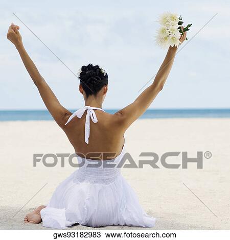 Rear view of a young woman sitting on the beach with her hands raised View Large Photo Image Stock Image - Rear view of a young woman sitting on the beach with her hands raised . Fotosearch