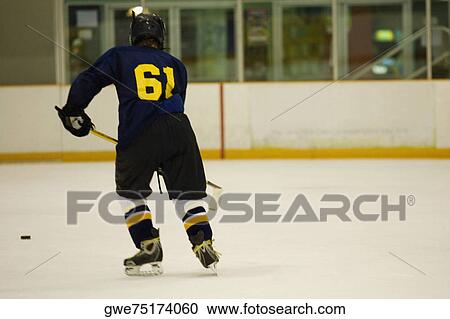Stock Image - Rear view of an ice hockey player playing ice hockey. Fotosearch