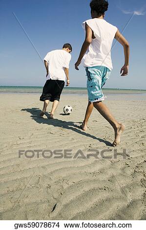 Rear view of two boys playing with a soccer ball on the beach View Large Photo Image Picture - Rear view of two boys playing with a soccer ball on the beach. Fotosearch