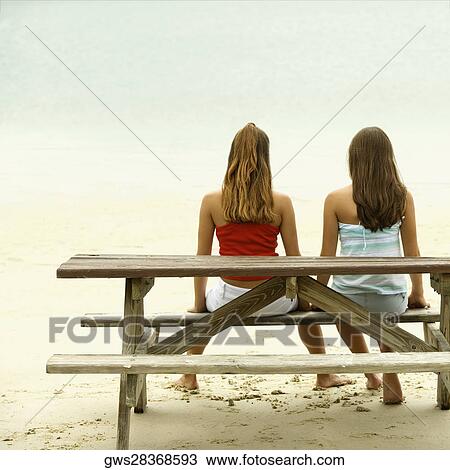 Rear view of two girls sitting on a bench at the beach View Large Photo Image Stock Image - Rear view of two girls sitting on a bench at the beach. Fotosearch