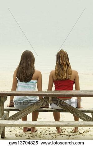 Rear view of two girls sitting on a bench at the beach View Large Photo Image Stock Photography - Rear view of two girls sitting on a bench at the beach. Fotosearch