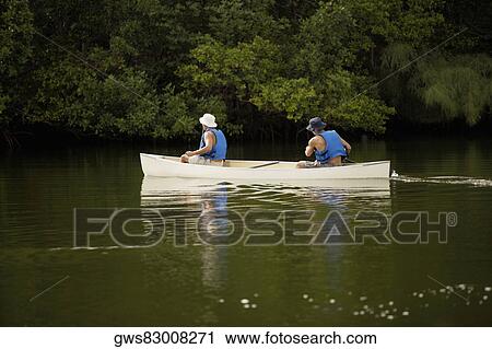Stock Image - Rear view of two people boating in a river. Fotosearch