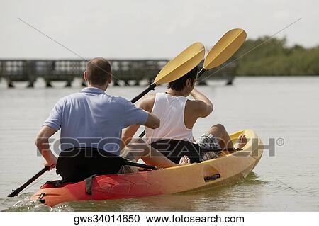 Stock Image - Rear view of two young men kayaking. Fotosearch