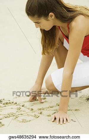 Side profile of a girl writing in sand View Large Photo Image Picture - Side profile of a girl writing in sand. Fotosearch