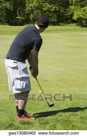 Stock Image - Side profile of a man holding a golf club on a golf course. Fotosearch
