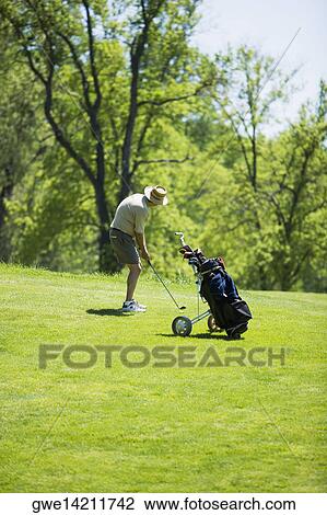 Stock Image - Side profile of a man holding a golf club on a golf course. Fotosearch