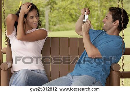 Stock Image - Side profile of a mid adult man photographing a young woman. Fotosearch