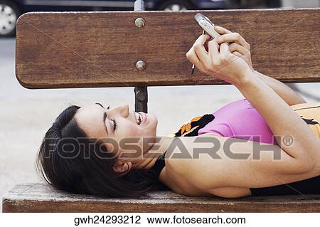 Side profile of a mid adult woman lying on a bench and using a personal data assistant View Large Photo Image Stock Image - Side profile of a mid adult woman lying on a bench and using a personal data assistant . Fotosearch