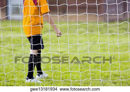 Side profile of a soccer player standing behind a net View Large Photo Image Picture - Side profile of a soccer player standing behind a net. Fotosearch