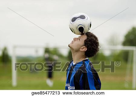 Stock Image - Side profile of a soccer player balancing a soccer ball on his forehead. Fotosearch