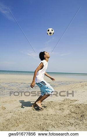Stock Photograph - Side profile of a teenage boy playing with a soccer ball on the beach. Fotosearch
