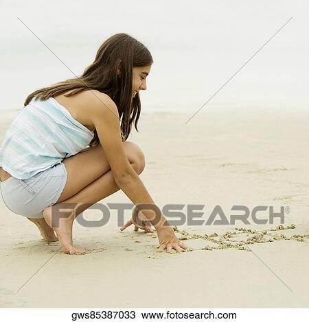 Stock Image - Side profile of a teenage girl writing in sand. Fotosearch
