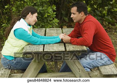 Side profile of a young couple sitting and holding hands View Large Photo Image Picture - Side profile of a young couple sitting and holding hands. Fotosearch