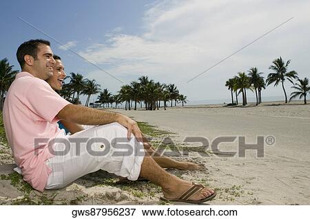 Side profile of a young couple smiling and sitting together on the beach View Large Photo Image Stock Photo - Side profile of a young couple smiling and sitting together on the beach. Fotosearch