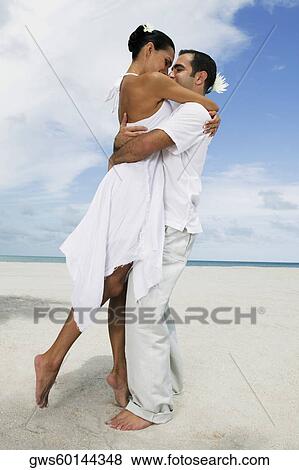 Stock Photo - Side profile of a young couple embracing each other on the beach. Fotosearch