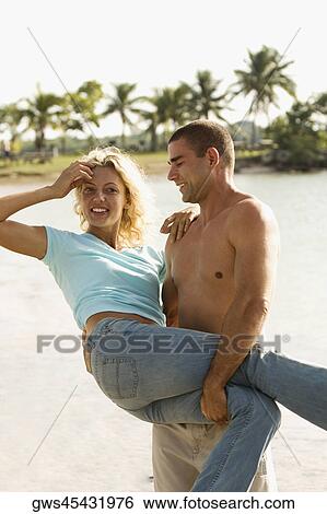 Side profile of a young man carrying a young woman on the beach View Large Photo Image Stock Photograph - Side profile of a young man carrying a young woman on the beach. Fotosearch