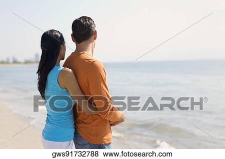 Stock Photo - Side profile of a young woman embracing a young man from behind. Fotosearch