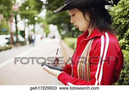 Side profile of a young woman holding a personal data assistant View Large Photo Image Stock Image - Side profile of a young woman holding a personal data assistant . Fotosearch