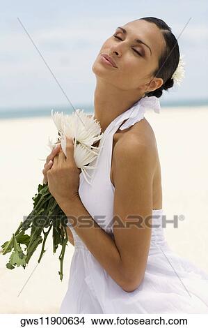 Picture - Side profile of a young woman holding flowers on the beach. Fotosearch