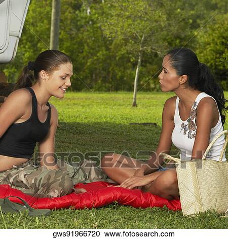 Stock Image - Side profile of a young woman sitting with a teenage girl and smiling. Fotosearch