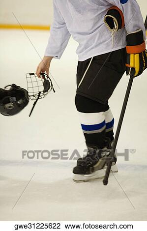 Stock Image - Side profile of an ice hockey player holding an ice hockey skate and a helmet. Fotosearch