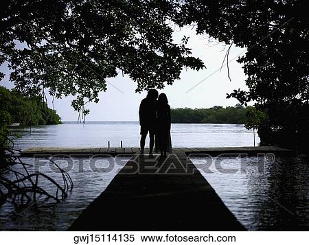 Stock Photography - Silhouette of a man and a woman standing on a pier. Fotosearch