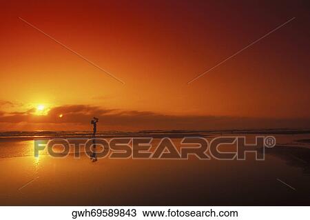 Stock Image - Silhouette of a person carrying a baby on the beach. Fotosearch