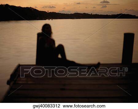 Silhouette of a young woman sitting on pier View Large Photo Image Stock Image - Silhouette of a young woman sitting on pier. Fotosearch