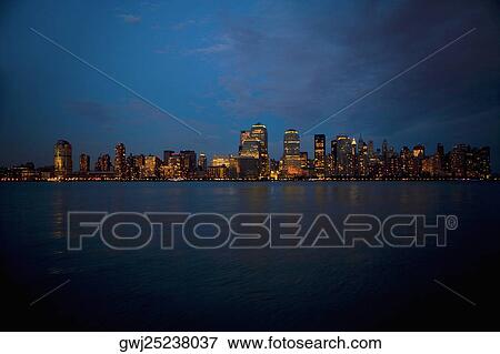 Stock Photo - Skyscrapers at the waterfront lit up at night, New York City, New York State, USA. Fotosearch
