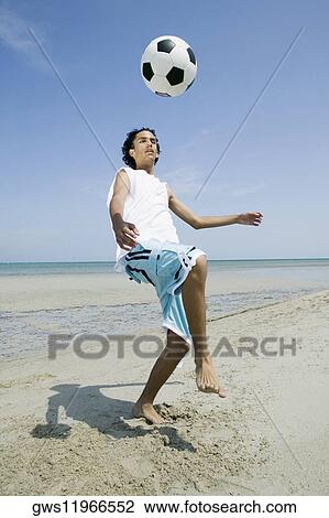 Stock Image - Teenage boy playing with a soccer ball on the beach. Fotosearch
