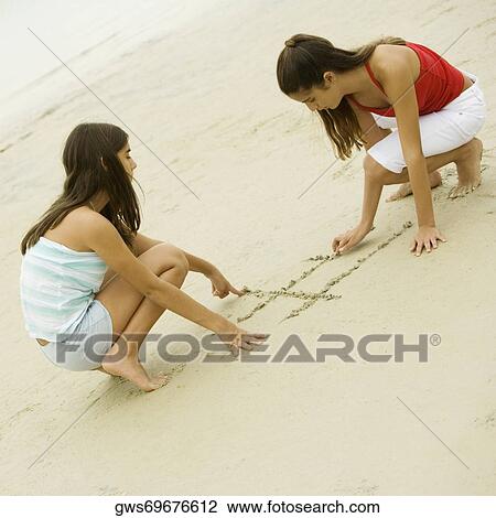 Stock Image - Two girls drawing in sand. Fotosearch
