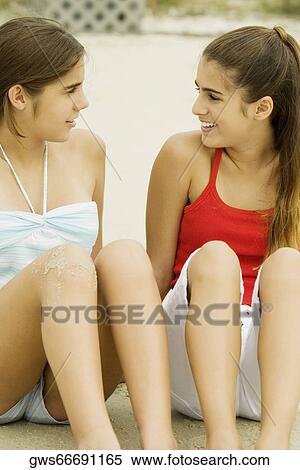 Stock Photography - Two girls sitting in sand at the beach. Fotosearch