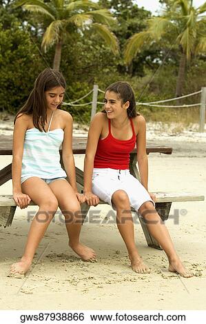 Two girls sitting on a bench at the beach View Large Photo Image Stock Photograph - Two girls sitting on a bench at the beach. Fotosearch