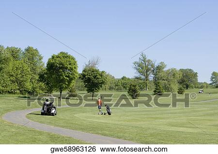 Stock Photograph - Two people and a golf cart on a golf course. Fotosearch