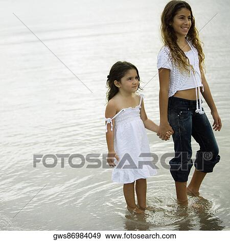Stock Photo - Two sisters holding hands standing in water. Fotosearch