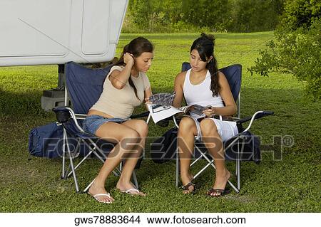 Two teenage girls sitting in armchairs and reading a magazine View Large Photo Image Picture - Two teenage girls sitting in armchairs and reading a magazine. Fotosearch