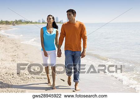 Stock Image - Young woman and a mid adult man walking on the beach. Fotosearch
