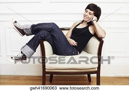 Young woman reclining in an armchair and talking on a mobile phone View Large Photo Image Stock Image - Young woman reclining in an armchair and talking on a mobile phone. Fotosearch