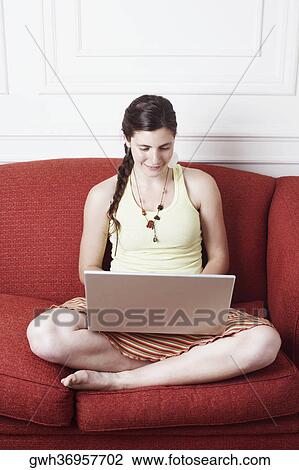 Young woman sitting on a couch and using a laptop View Large Photo Image Stock Image - Young woman sitting on a couch and using a laptop. Fotosearch
