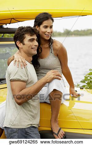 Young woman sitting on the bonnet of a jeep with her arm over a mid adult man View Large Photo Image Stock Photography - Young woman sitting on the bonnet of a jeep with her arm over a mid adult man. Fotosearch