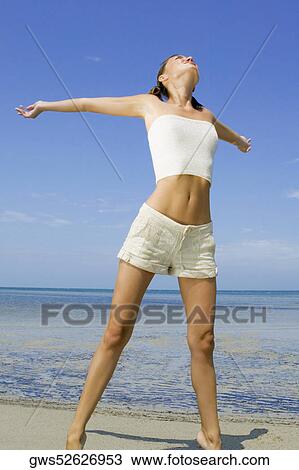 Stock Image - Young woman standing on the beach with her arms outstretched. Fotosearch