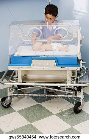 Picture - Boy touching a baby boy in an incubator. Fotosearch