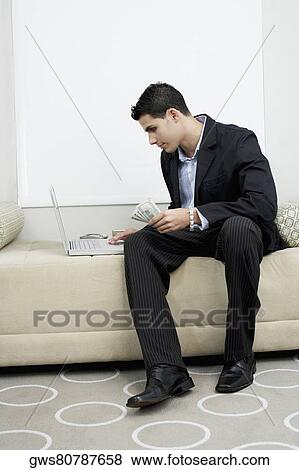 Businessman holding US paper currency and using a laptop View Large Photo Image Stock Photo - Businessman holding US paper currency and using a laptop. Fotosearch