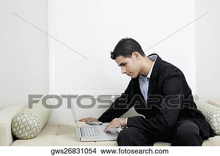 Businessman using a laptop on a couch View Large Photo Image Picture - Businessman using a laptop on a couch. Fotosearch