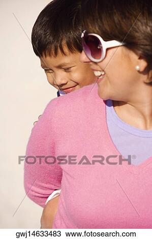 Stock Image - Close-up of a boy riding piggyback on his mother. Fotosearch