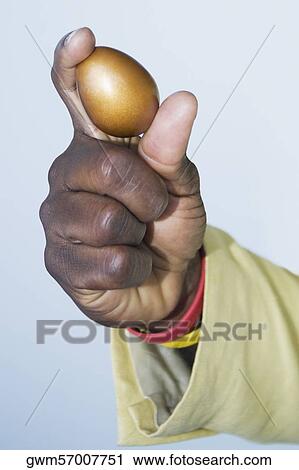 Stock Image - Close-up of a human hand holding a golden egg. Fotosearch