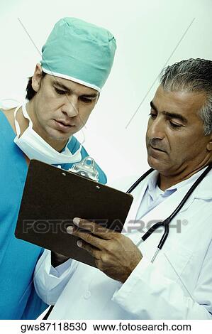 Close-up of a male doctor discussing a report with a surgeon View Large Photo Image Stock Image - Close-up of a male doctor discussing a report with a surgeon. Fotosearch