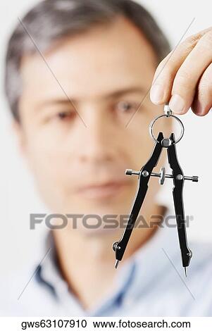 Close-up of a mature man holding a drawing compass in front of his face View Large Photo Image Stock Image - Close-up of a mature man holding a drawing compass in front of his face. Fotosearch